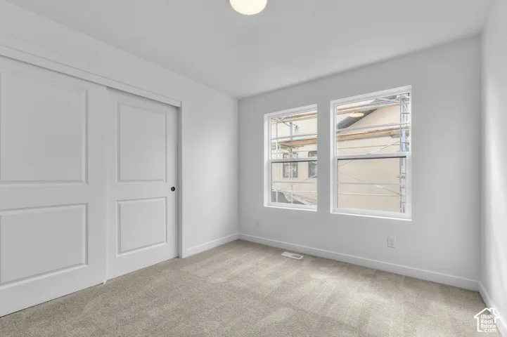Room featuring neutral-toned carpeting, dual-pane windows with white frames, and a two-panel sliding closet door