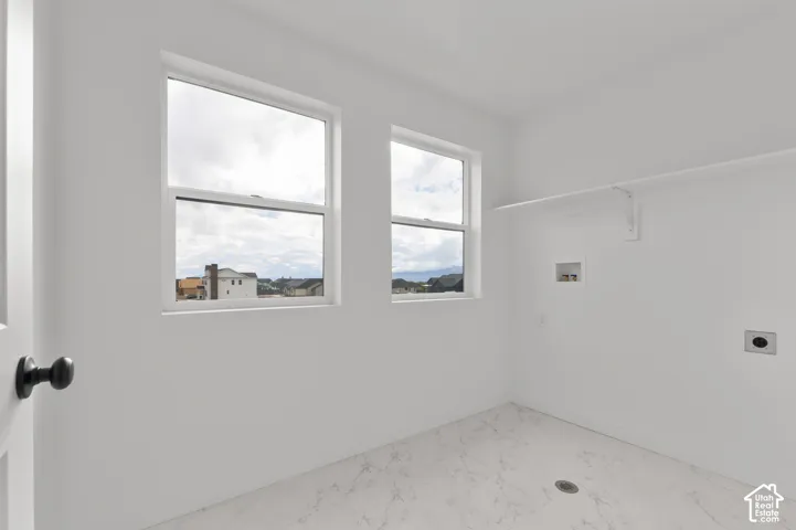 Room featuring dual windows, stone-patterned tile flooring, a wall-mounted shelving unit, and plumbing hookups