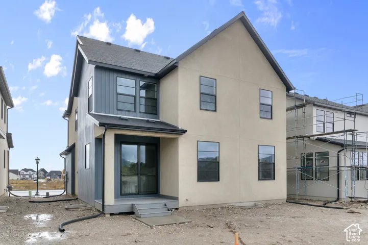 Multi-story exterior featuring a mixed-material facade of stucco and board-and-batten siding, asphalt shingle roofing, and rear-entry sliding glass doors