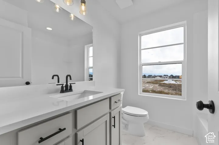 Light-toned vanity featuring a solid surface countertop, undermount sink, matte black faucet hardware, and a large frameless mirror with industrial-style light fixtures