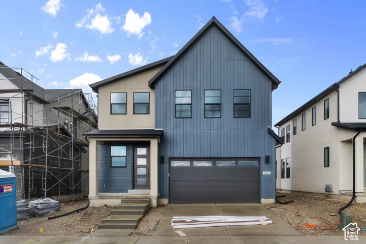 Two-story exterior featuring vertical blue siding, a neutral-toned stucco finish, a concrete front entry staircase, and an attached two-car garage with a paneled door