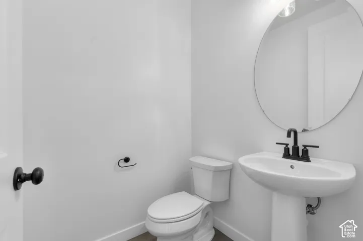 Pedestal sink with a matte black centerset faucet, round frameless mirror, and matching matte black hardware