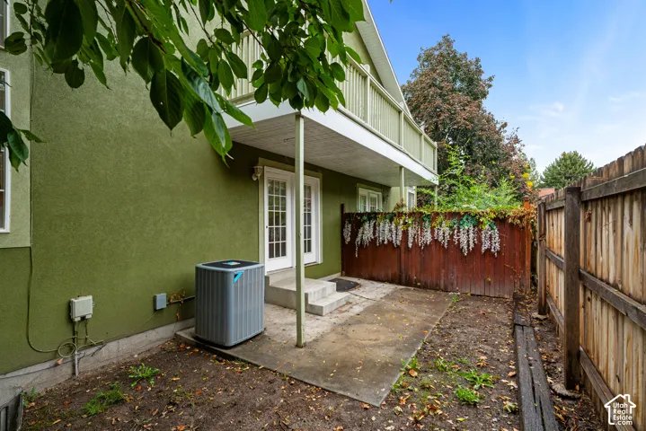 Stucco exterior featuring a concrete patio, wood-slat privacy fencing, French doors, and an elevated wooden balcony
