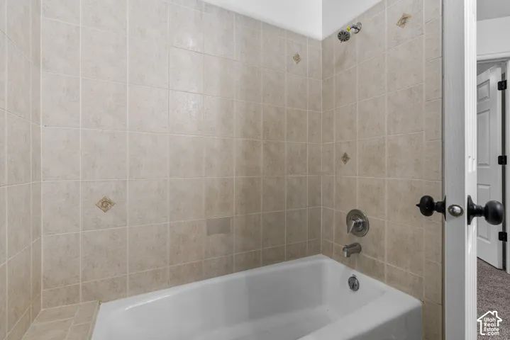 Bathtub enclosure featuring neutral ceramic wall tile, decorative accent tiles, a polished chrome mixing valve, and a wall-mounted shower head