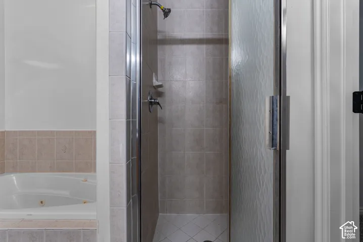 Soaking tub with tile surround and separate shower enclosure featuring glass door and tile wall surfacing