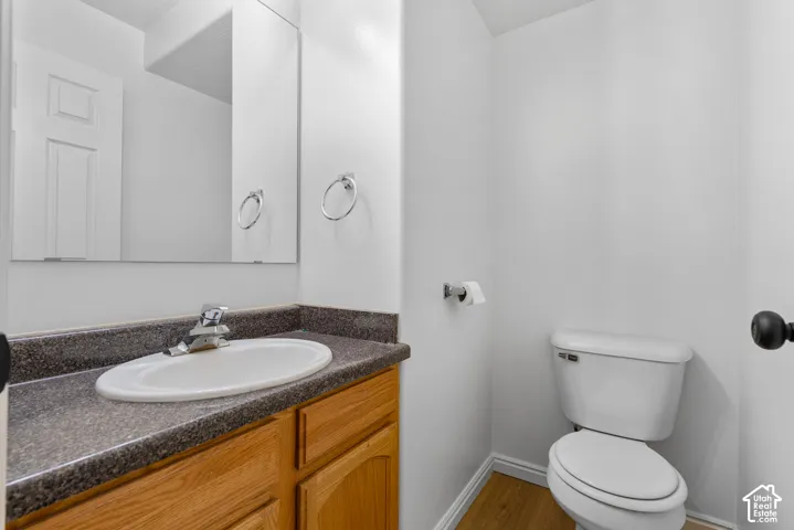 Single-sink vanity with a speckled countertop, undermount oval basin, wood-finish cabinetry, wall-mounted mirror, and wood-finish flooring