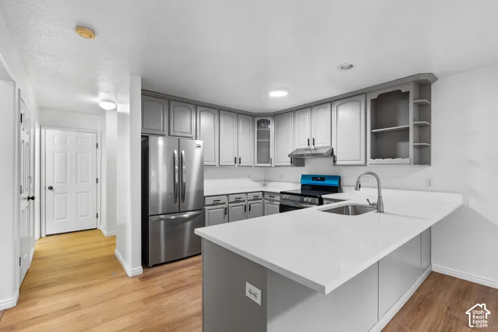 Kitchen featuring gray cabinetry, solid-surface countertops, stainless steel refrigerator, undermount sink with gooseneck faucet, and wood-finish flooring
