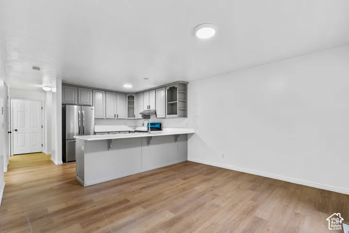 Kitchen featuring grey shaker-style cabinetry, white countertops, a breakfast bar, and wood-finish flooring