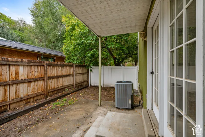 Covered concrete patio featuring glass-paneled doors, wood-slat perimeter fencing, and white vinyl privacy screening