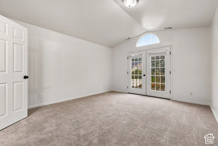 Vaulted ceiling with an arched window, neutral wall-to-wall carpeting, and double glass-pane doors