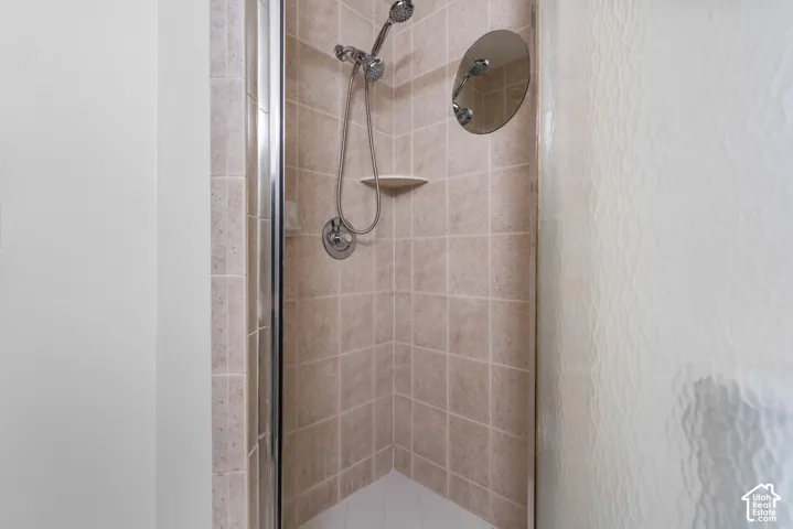 Shower enclosure featuring neutral tile wall surrounds, a chrome handheld shower fixture, an integrated corner shelf, and textured glass doors