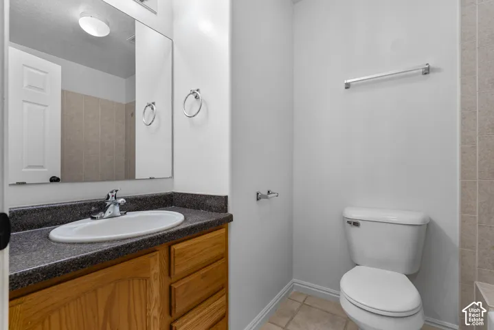 Bathroom featuring a wood-finish vanity with a stone-composite countertop, integrated oval sink, wall-mounted mirror, and tile flooring
