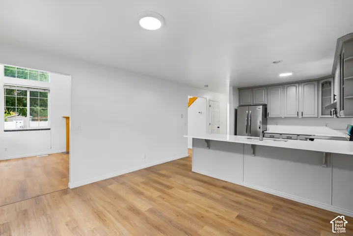 Kitchen featuring light-toned cabinetry, a peninsula with a solid-surface countertop, stainless steel refrigerator, and wood-finish flooring