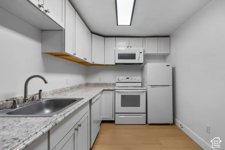 Kitchen featuring white shaker-style cabinetry, speckled stone-finish countertops, stainless steel sink with high-arc faucet, integrated white appliances, and wood-finish flooring