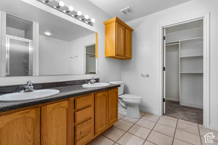 Dual-sink vanity with dark stone-finish countertop, wood cabinetry, wall-to-wall mirror, and tile flooring