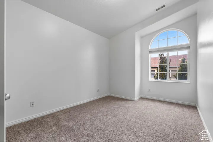 Neutral-toned carpeting, vaulted ceiling, and an arched window featuring a dual-pane design