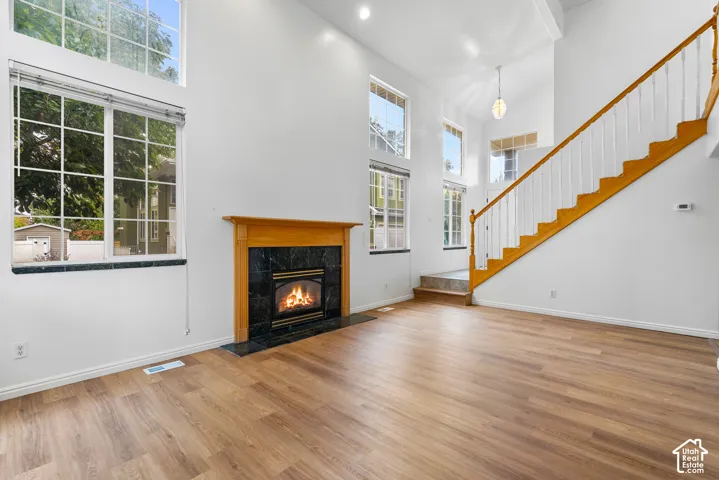 Vaulted ceilings, large windows, wood-finish flooring, a fireplace with a stone-surround mantle, and a wooden staircase with white spindles
