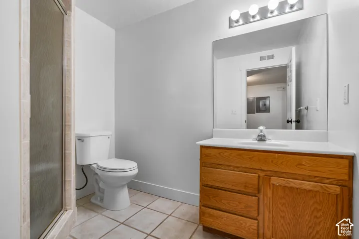 Bathroom featuring a wood-finish vanity with a white countertop, inset sink, large wall-mounted mirror, four-light fixture, and ceramic tile flooring