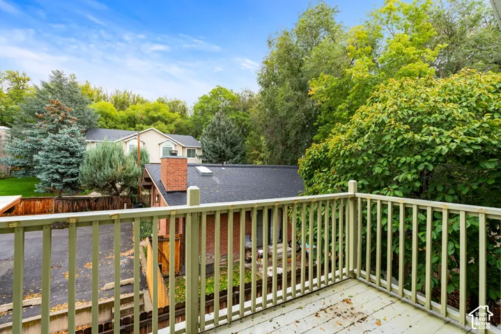 Elevated deck with wooden railings, brick-exterior building, shingled roofing, skylight, and mature tree landscaping