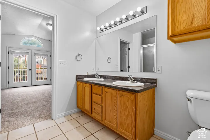 Dual-sink vanity with a solid-surface countertop, full-width vanity mirror, eight-bulb light fixture, wood-finish cabinetry, and ceramic tile flooring