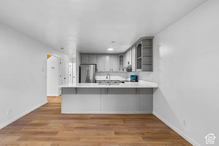 Kitchen featuring cabinetry with integrated shelving, stainless steel appliances, a peninsula with a solid-surface countertop, and wood-finish flooring