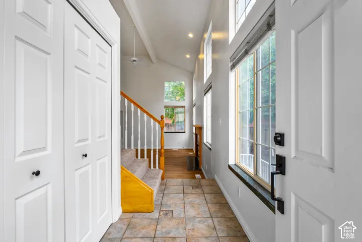Entryway featuring vaulted ceilings, floor-to-ceiling windows, tile flooring, and staircase with wood handrails