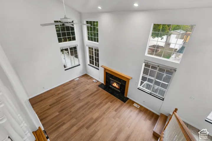 Vaulted ceilings featuring a ceiling fan, wood-finish flooring, multi-story windows, and a fireplace with a wood mantel and stone surround