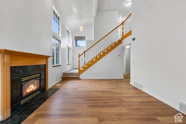 High-ceiling interior featuring wood-finish flooring, a fireplace with a stone-tile surround, and a wood-railing staircase
