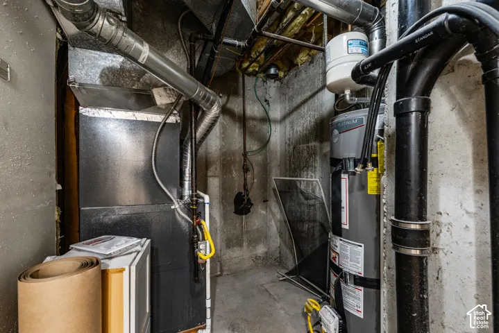 Utility area featuring a furnace, water heater, metal ductwork, and exposed concrete walls