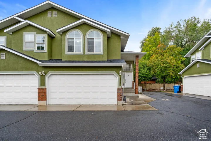 Multi-level exterior featuring stucco siding, brick veneer accents, arched windows, and two-car garage bays