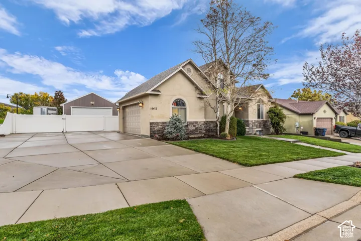 Exterior featuring stucco and stone veneer siding, an attached garage, a detached garage, a concrete driveway, and a fenced yard