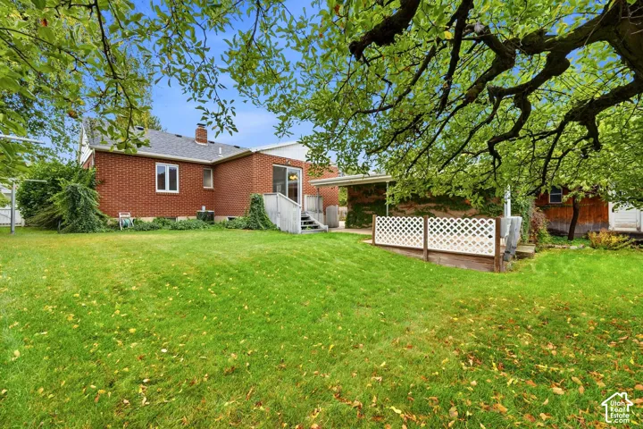 Brick exterior residence featuring a rear concrete patio with lattice privacy screen, covered carport, and expansive lawn area