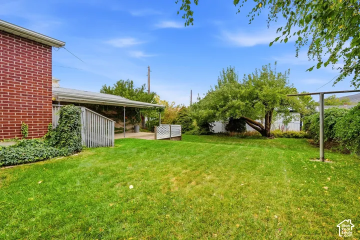 Red brick exterior featuring a covered patio, wooden decking, mature trees, and a spacious lawn