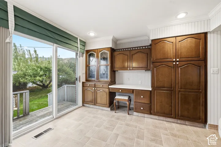 Built-in wood cabinetry with glass-panel upper doors, integrated desk workspace, tile flooring, beadboard wall paneling, and sliding glass doors