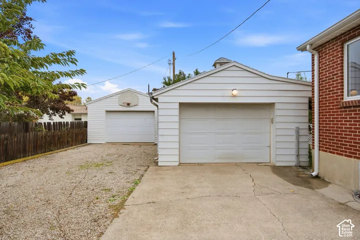 Detached garage with white horizontal siding, concrete parking apron, and gravel driveway