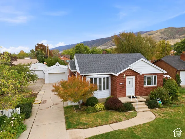 Brick exterior with a prominent bay window, asphalt shingle roof, detached garage, and mountain backdrop