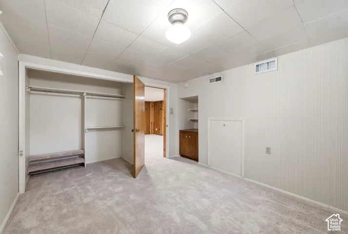 Interior space featuring wall-to-wall carpeting, a built-in reach-in closet with integrated shelving, ceiling-mounted light fixture, and a built-in lower storage cabinet with recessed open shelving
