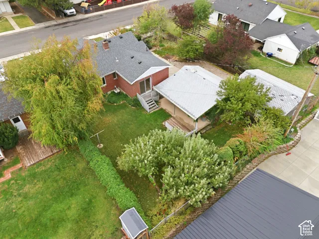 Aerial view of property featuring a brick exterior, shingled roofing, a covered patio, a detached structure, and mature landscaping