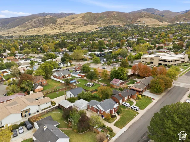Aerial perspective featuring established neighborhood surroundings, mature deciduous trees, and a backdrop of mountain terrain
