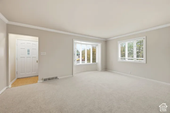 Neutral-toned interior space featuring crown molding, a multi-pane bay window, a standard rectangular window, and a multi-panel entry door