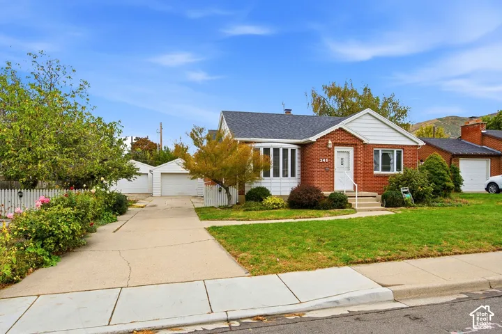 Brick exterior featuring a bay window, asphalt shingle roofing, concrete driveway, and detached garage