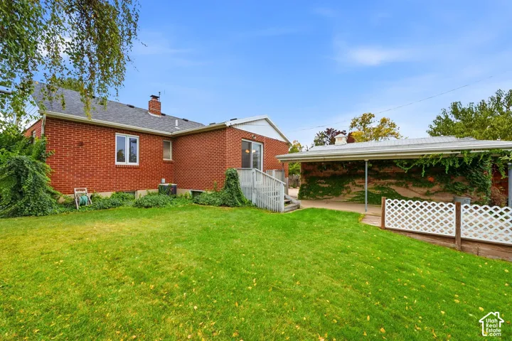 Red brick exterior featuring a multi-pitched shingle roof, a covered carport, a fenced lawn area, and a raised wooden deck