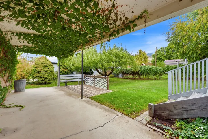Covered concrete patio featuring a wood-deck platform, lattice screen, and wooden staircase leading to the rear yard