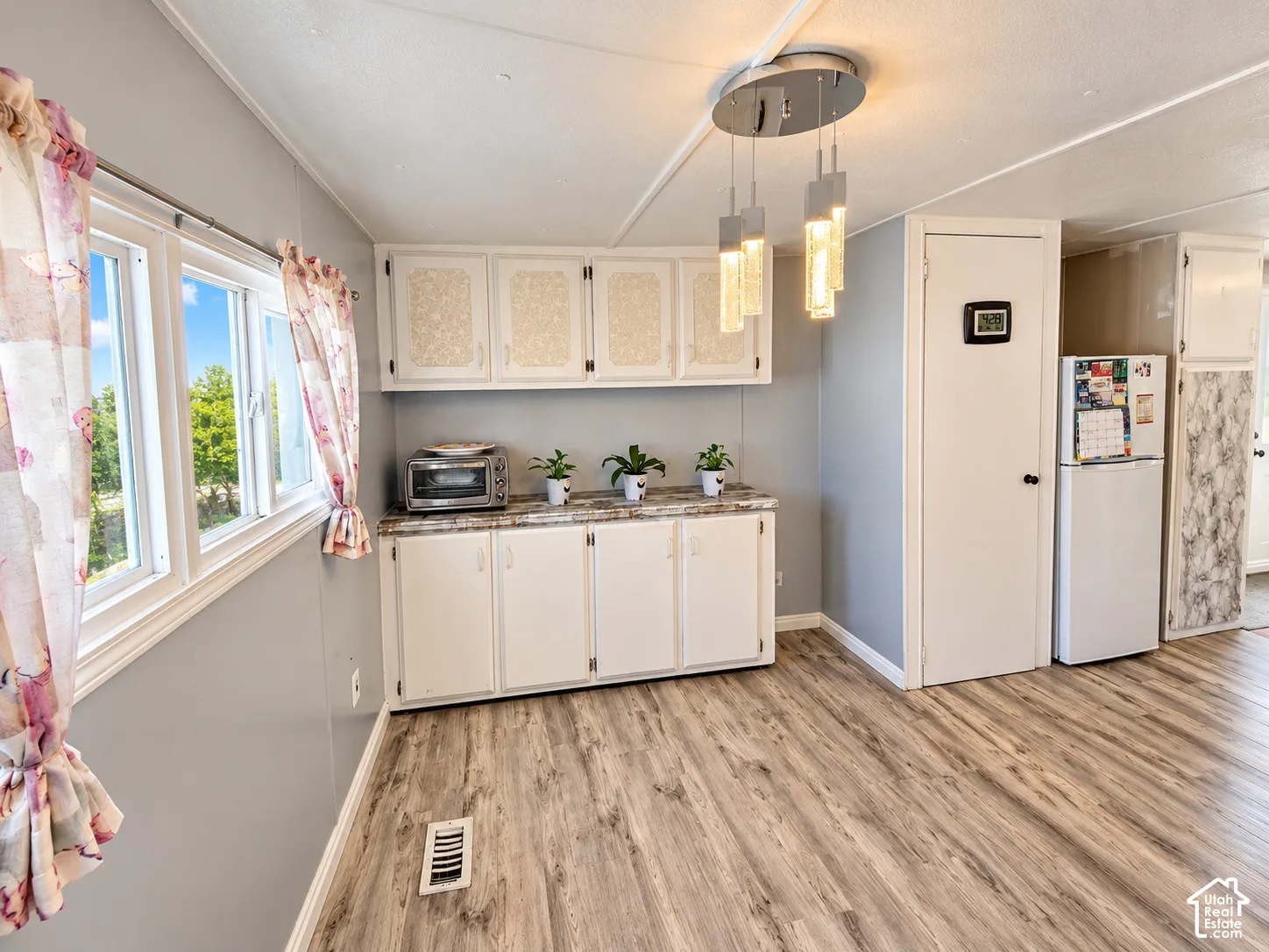 Kitchen area featuring white cabinetry with textured panel inserts, stone-finish countertops, wood-finish flooring, and a multi-pendant light fixture