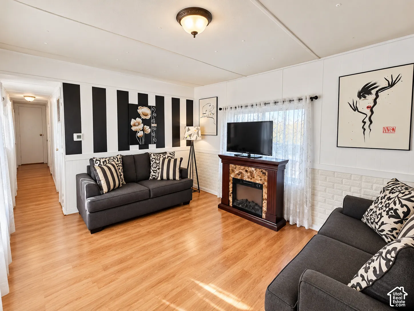 Living area featuring wood-finish flooring, a decorative fireplace mantle with a stone-style surround, accent wall paneling, and flush-mount ceiling lighting