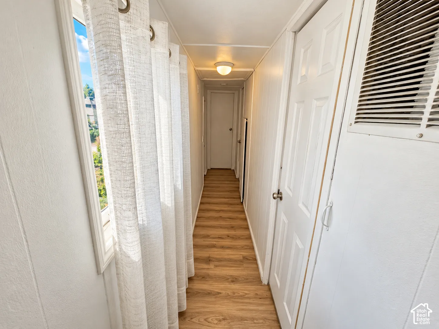 Hallway featuring wood-finish flooring, white panel walls, and flush-mount ceiling lighting