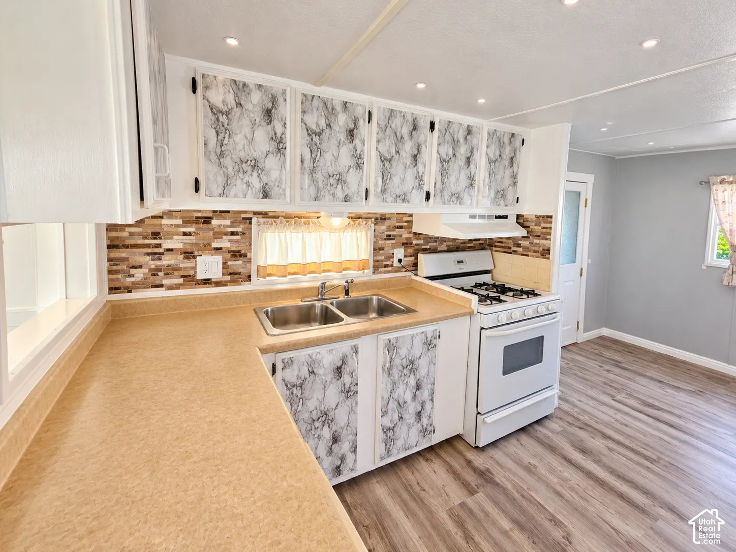 Kitchen featuring solid-surface countertops, patterned cabinetry, stainless steel dual-basin sink, tile backsplash, and wood-finish flooring