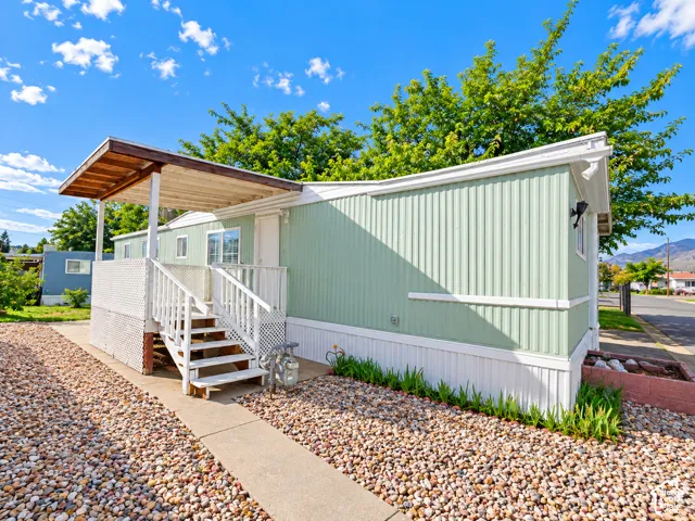 Exterior featuring light green vertical siding, a covered porch with white railing, and decorative stone landscaping
