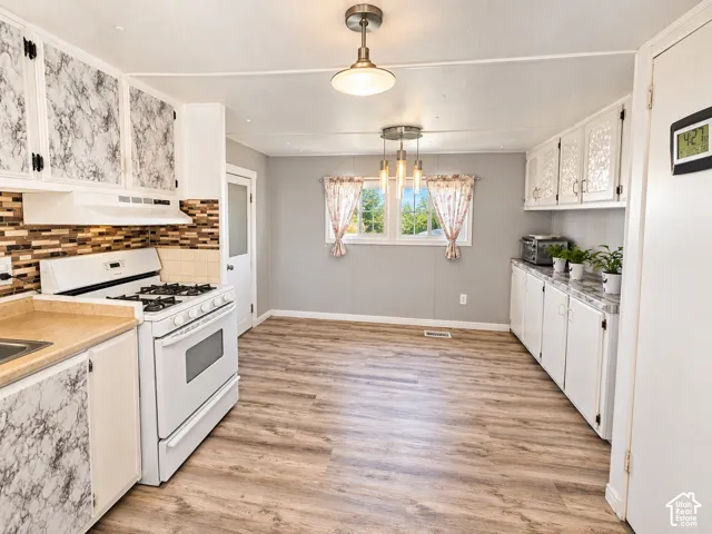 Kitchen featuring wood-finish flooring, white cabinetry with patterned inlay, a multi-tone tile backsplash, white gas range, and dual overhead light fixtures