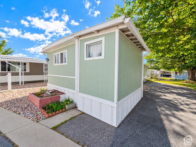 Exterior featuring vertical panel siding, a concrete walkway, a masonry-bordered planter, and an asphalt driveway